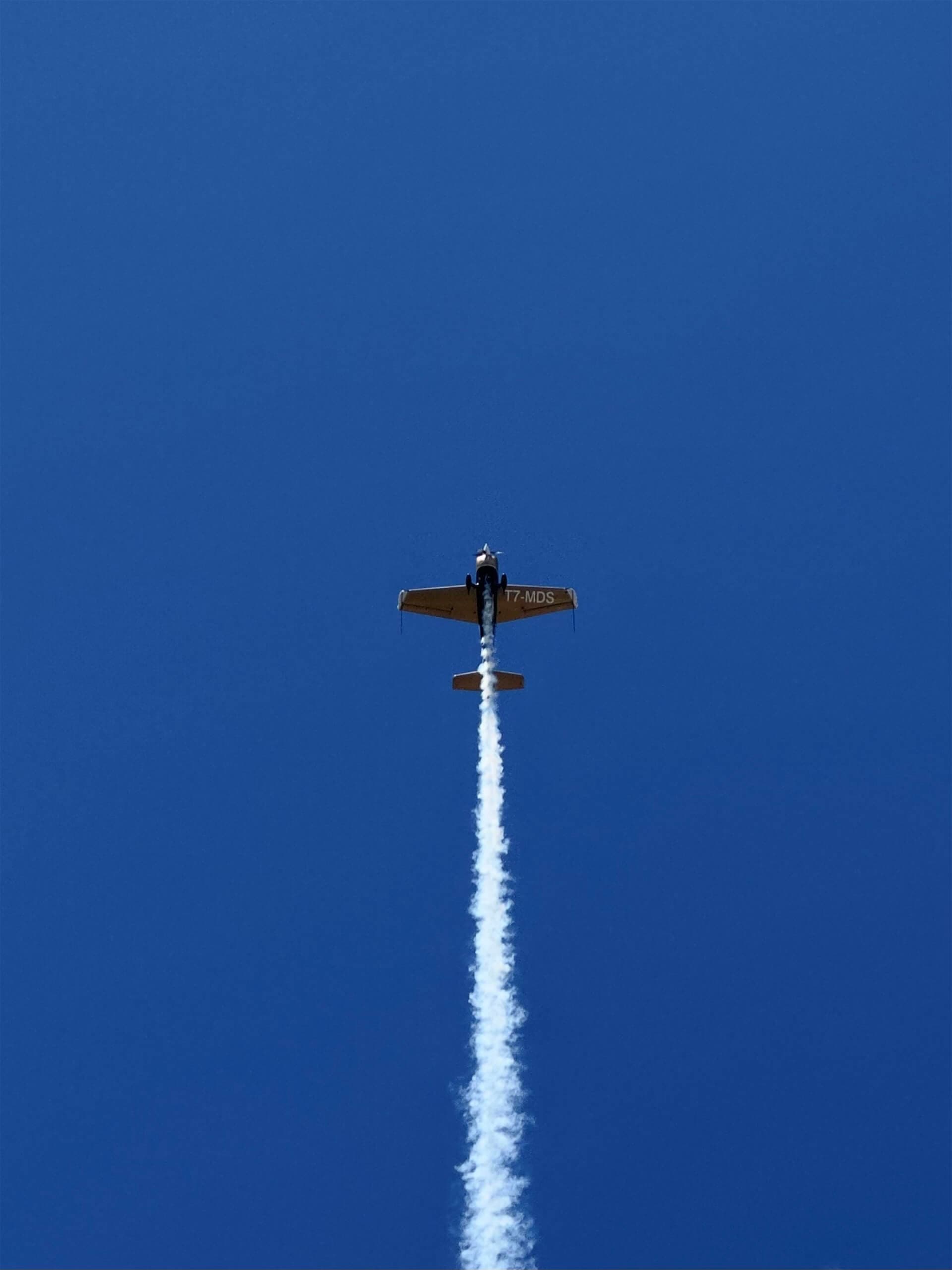 Aerobatic plane climbing vertically with a smoke trail against blue sky