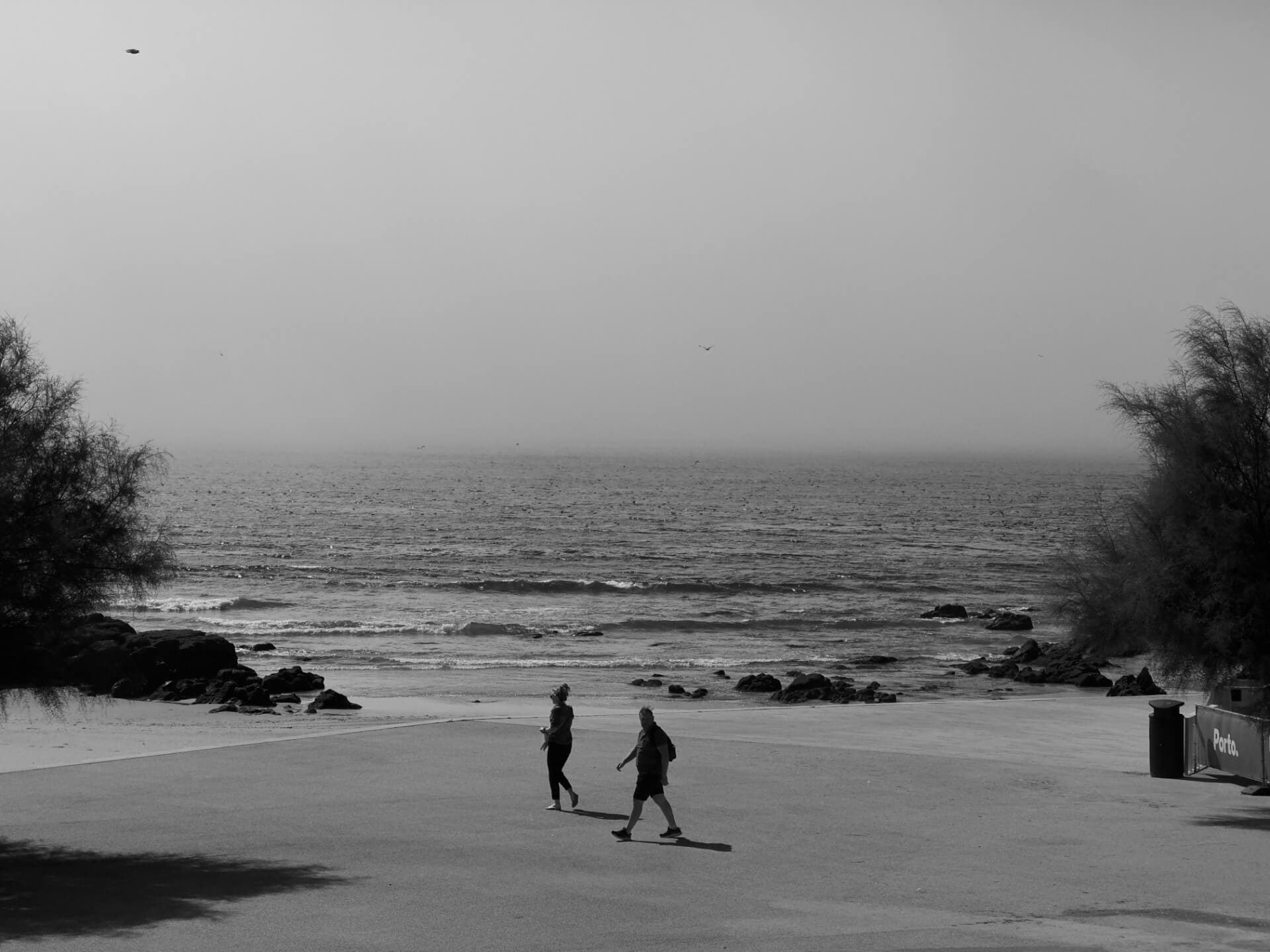 Two people walking along Porto beach in black and white