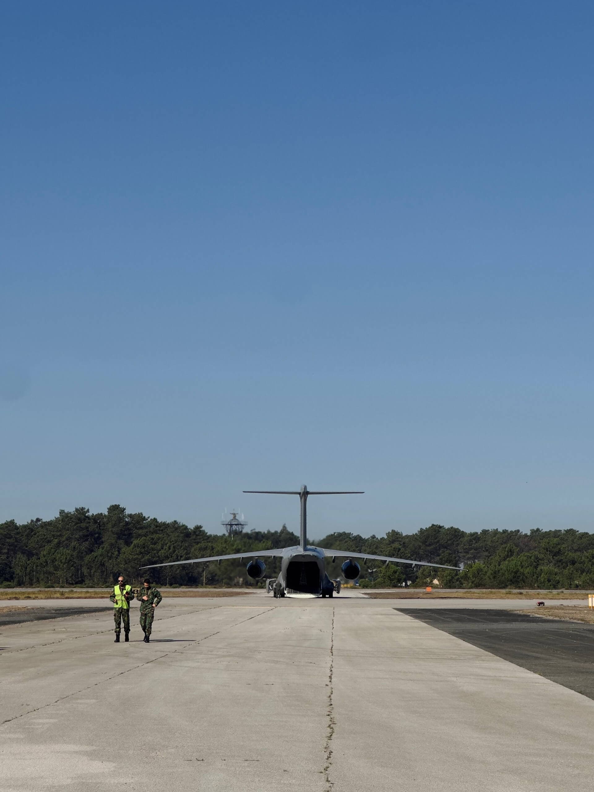 Military transport plane on a runway with two crew members walking