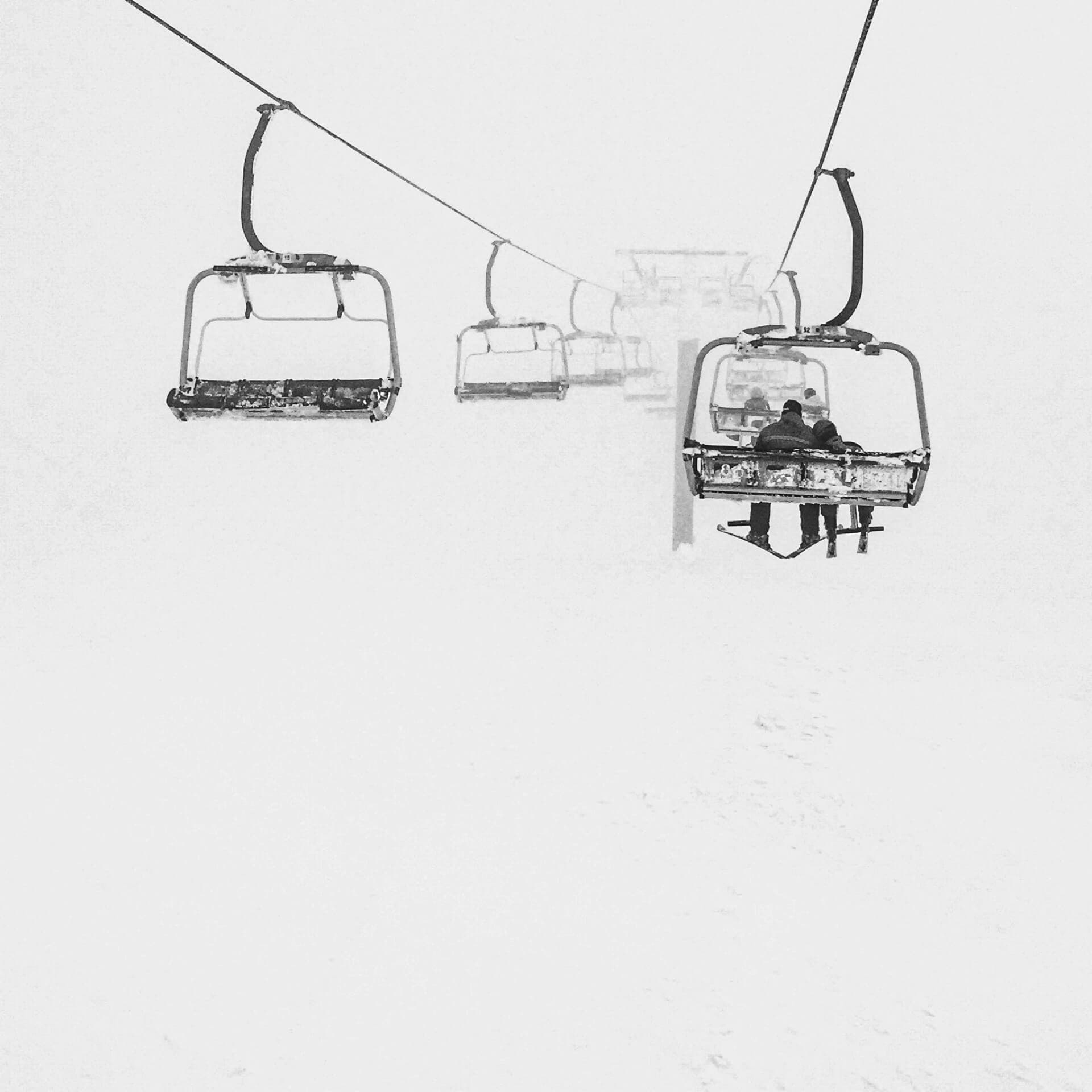 Ski chairlifts disappearing into fog and snow in black and white