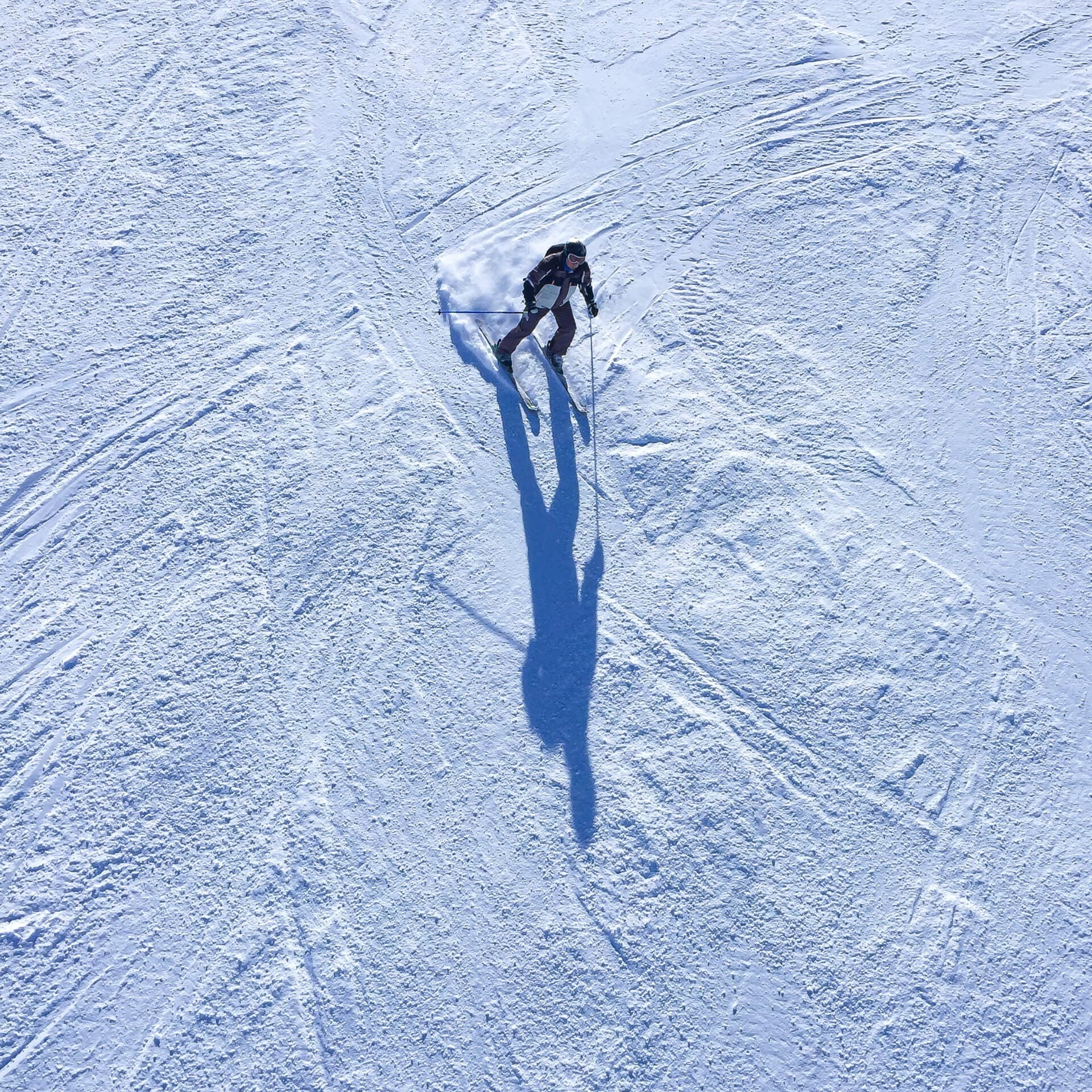 Lone skier casting a long shadow on snow seen from above