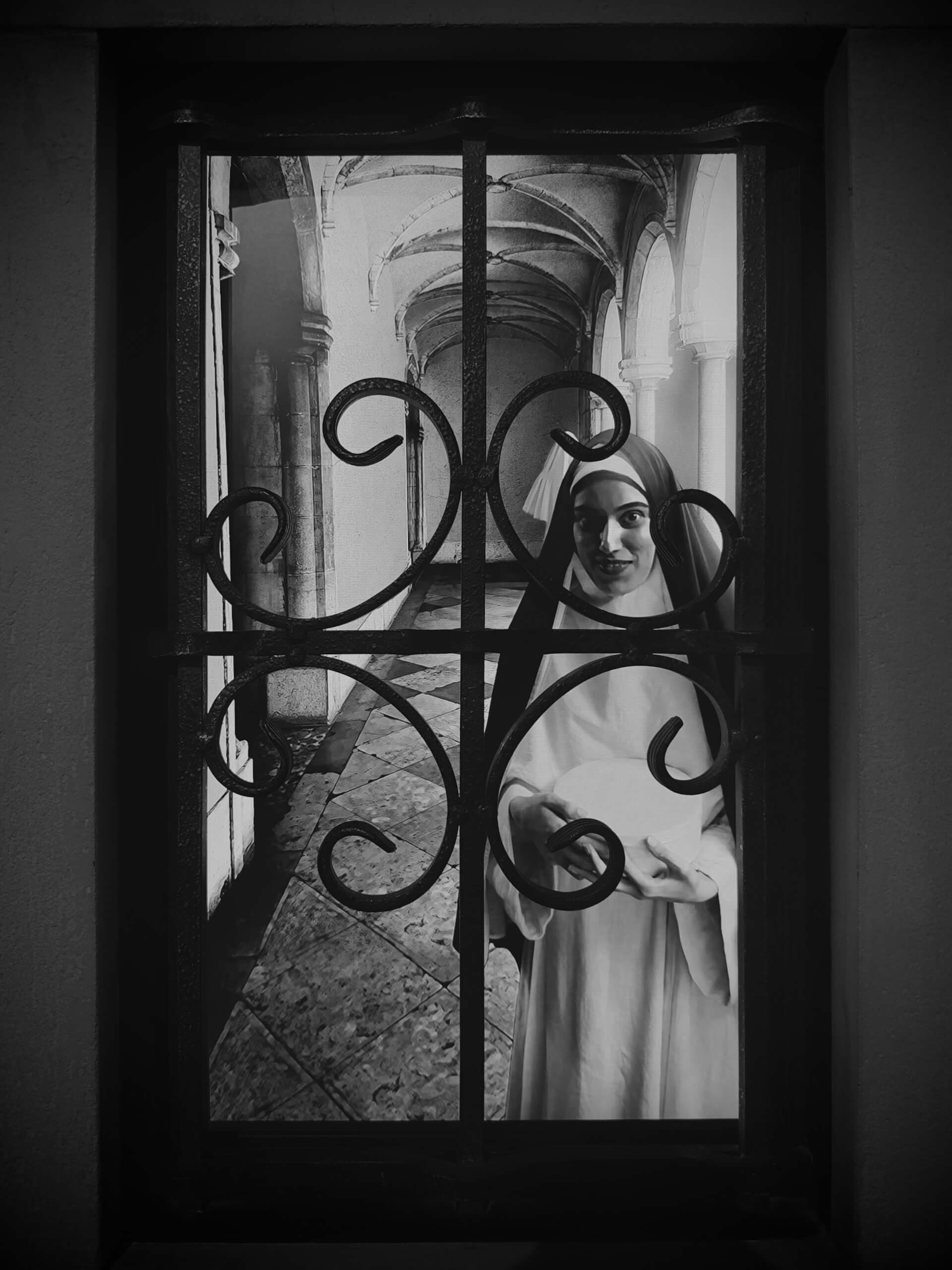 Religious figure seen through an ornate iron window grate in black and white