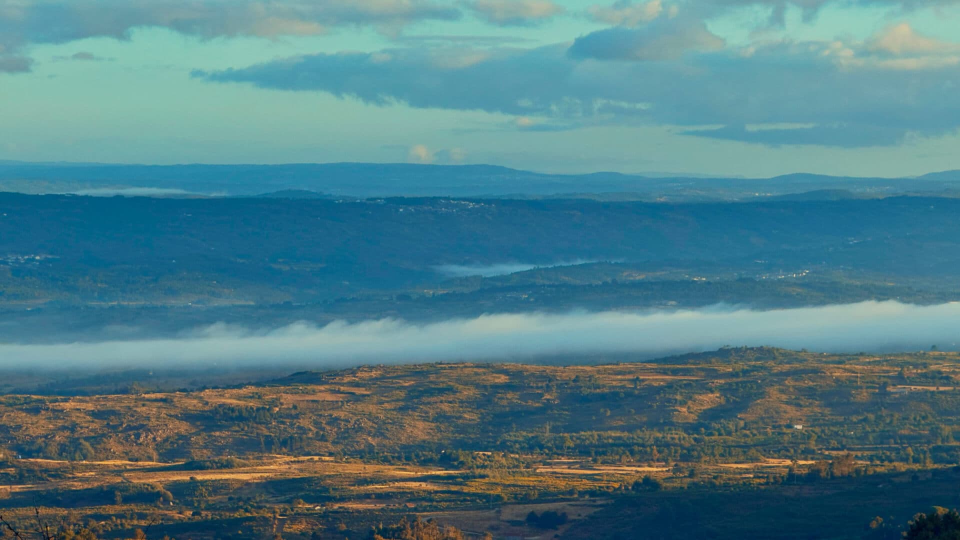 Morning fog rolling over a valley with layered green hills