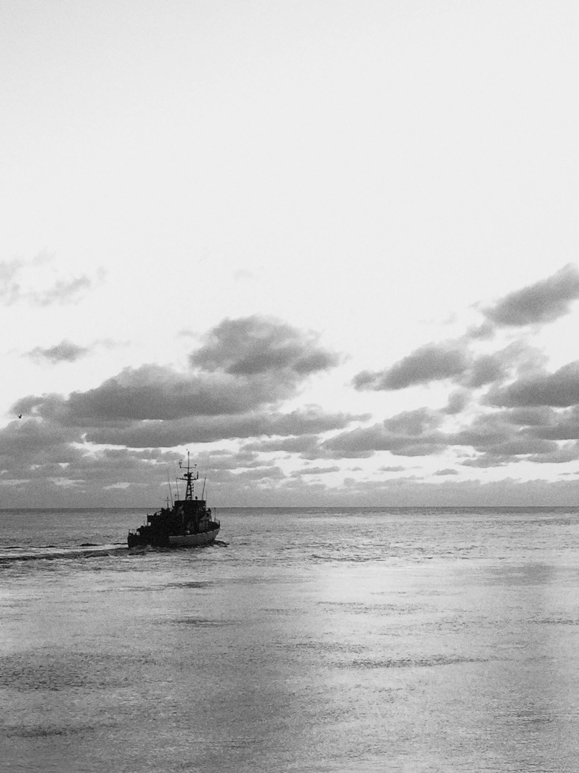 Fishing boat alone on the open sea under a cloudy sky in black and white