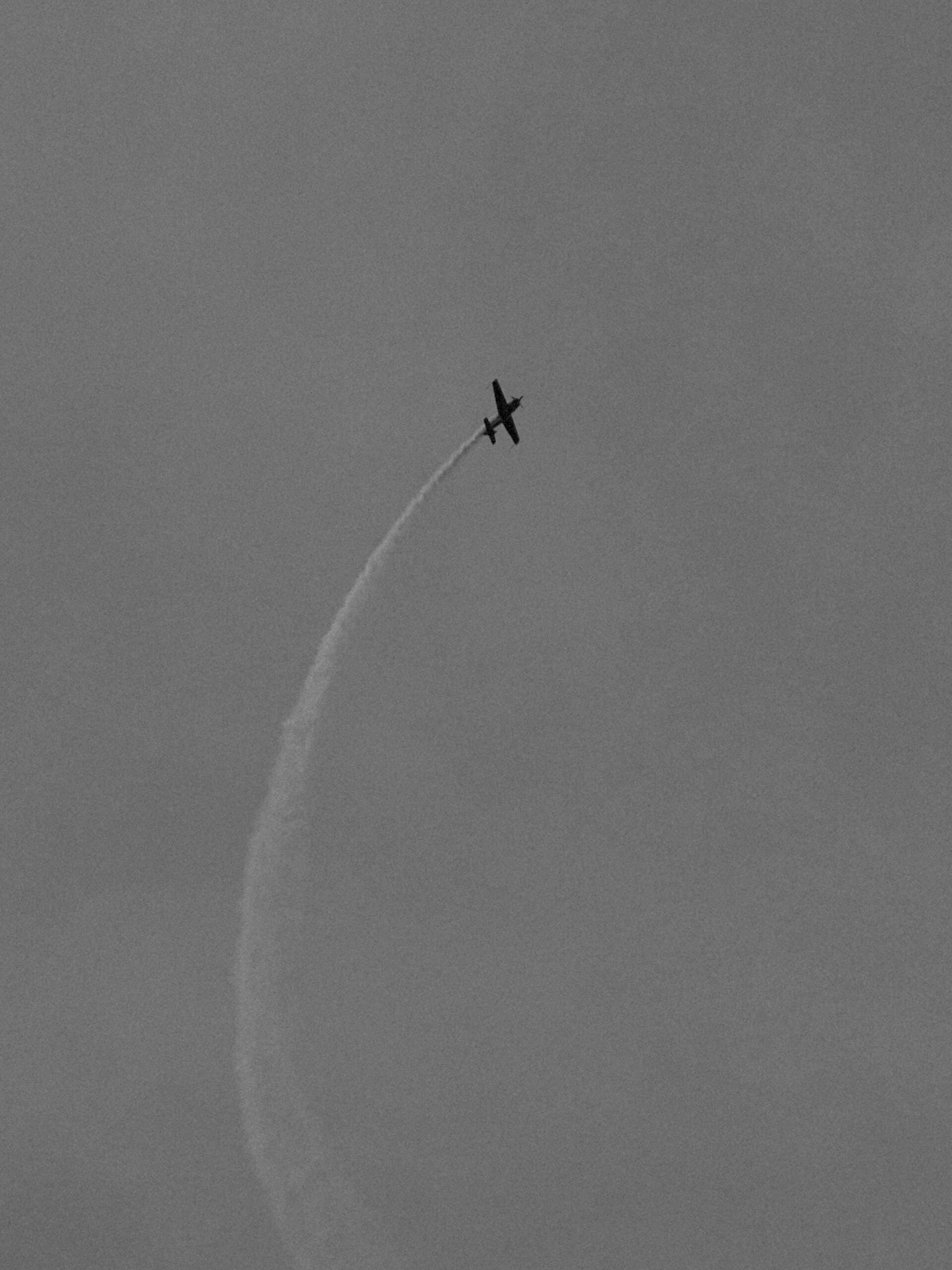 Aerobatic plane drawing a curved smoke trail across the sky in black and white