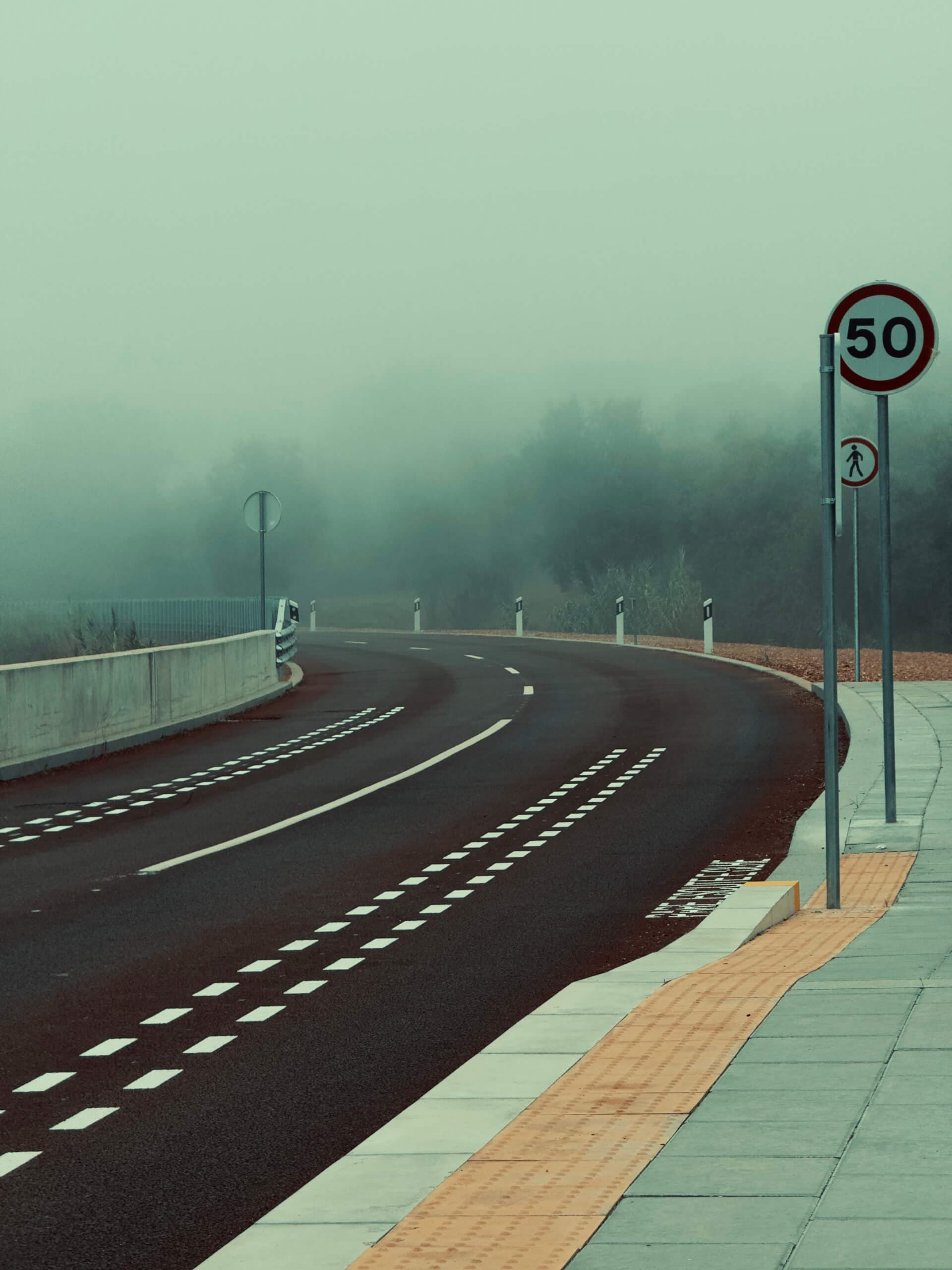 Foggy curved mountain road with a speed limit sign