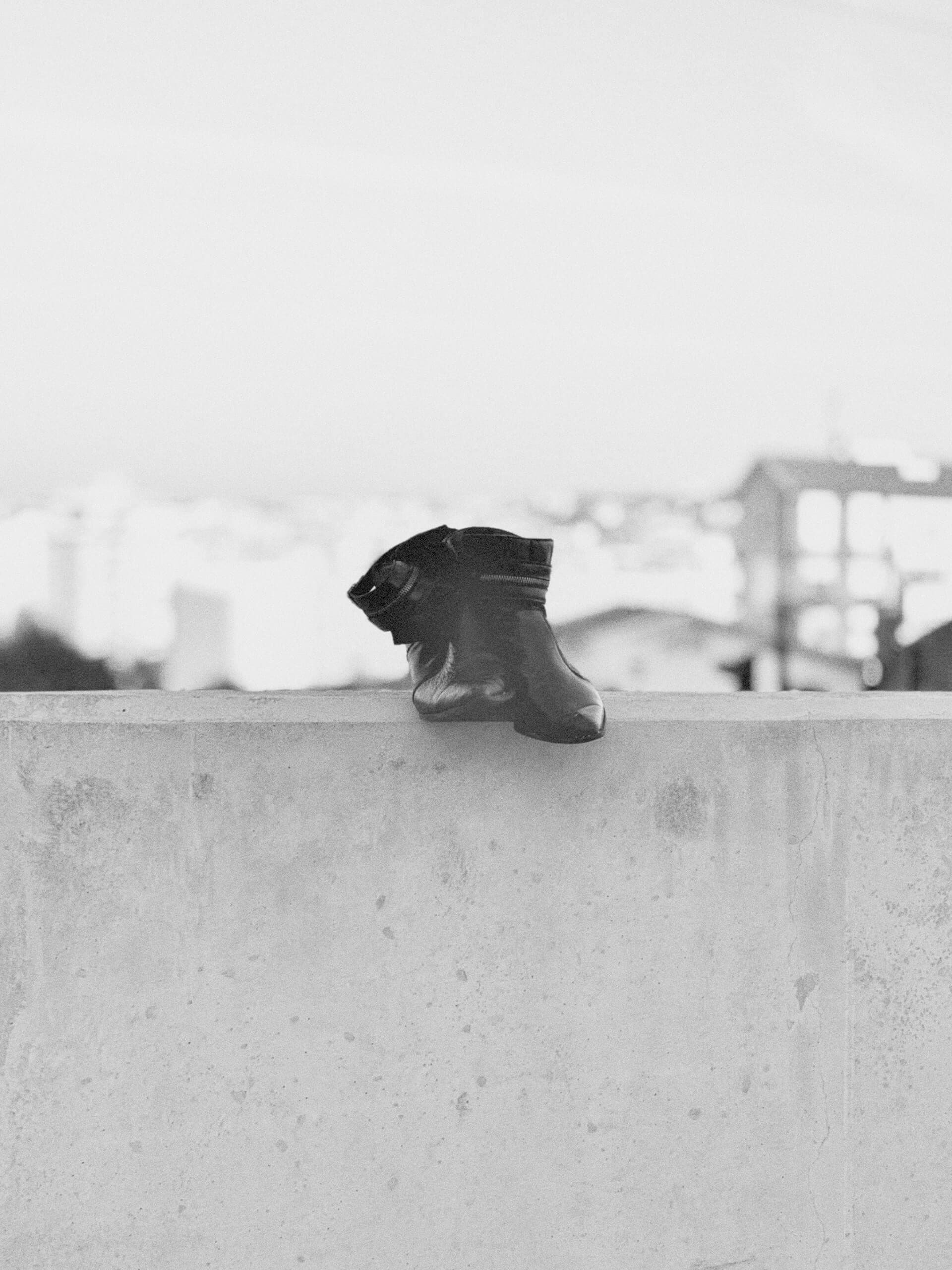 Lone boot perched on a concrete wall in black and white