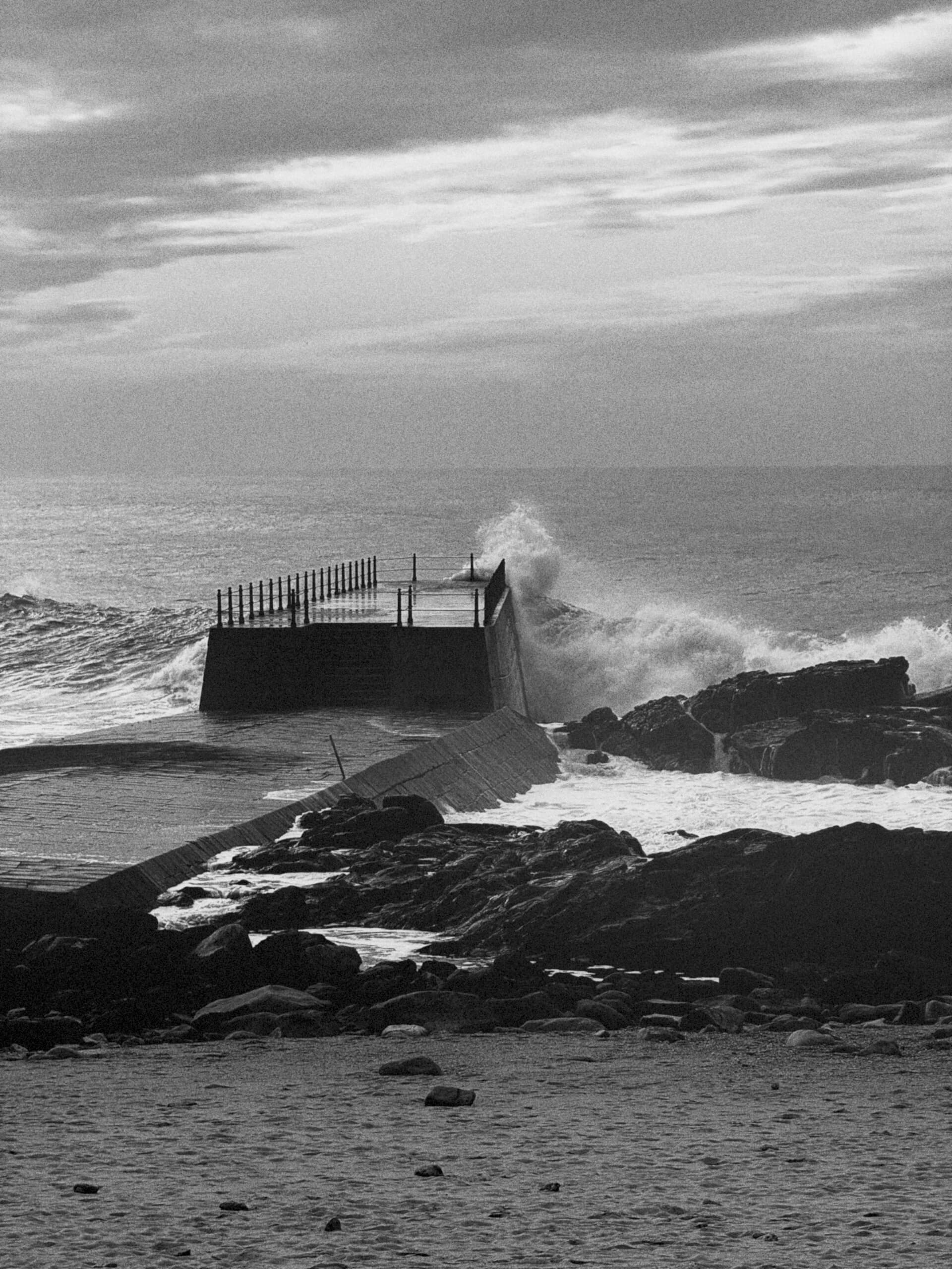 Ocean waves crashing against a concrete pier in black and white